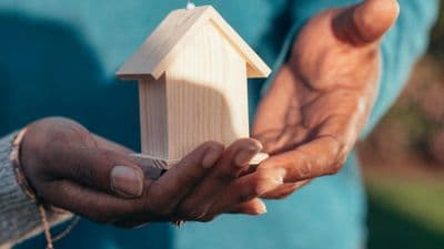 Diverse hands holding wooden house model symbolizing accessibility