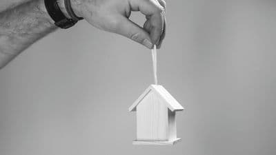 Hand holding suspended house model representing housing risk