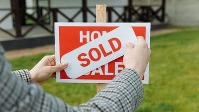 Person placing sold sticker on home for sale sign