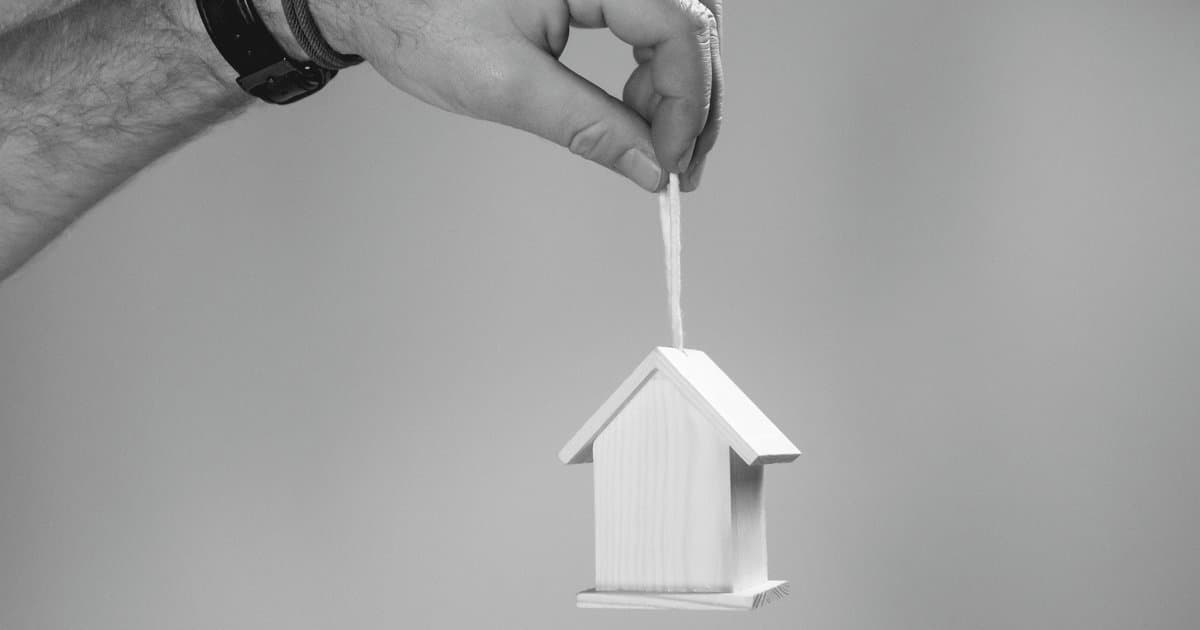 Hand holding suspended house model representing housing risk